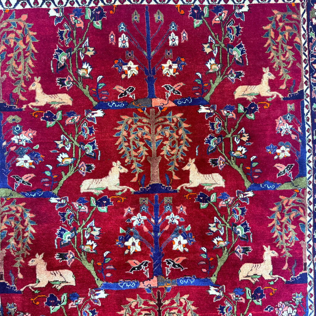 Decorative rug with intricate patterns of animals, trees, and flowers on a red background.