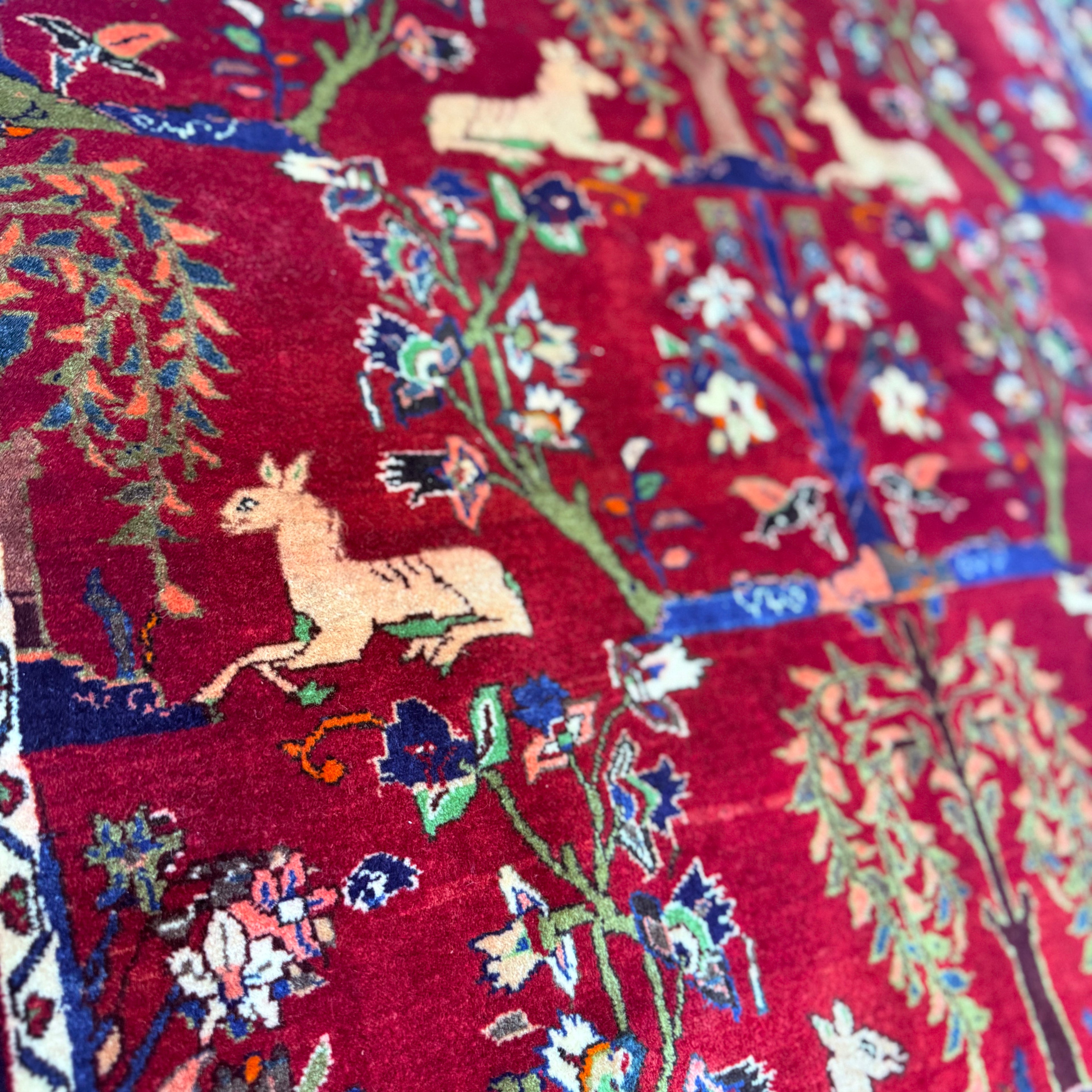 Close-up of a red fabric with intricate patterns including deer and floral designs.