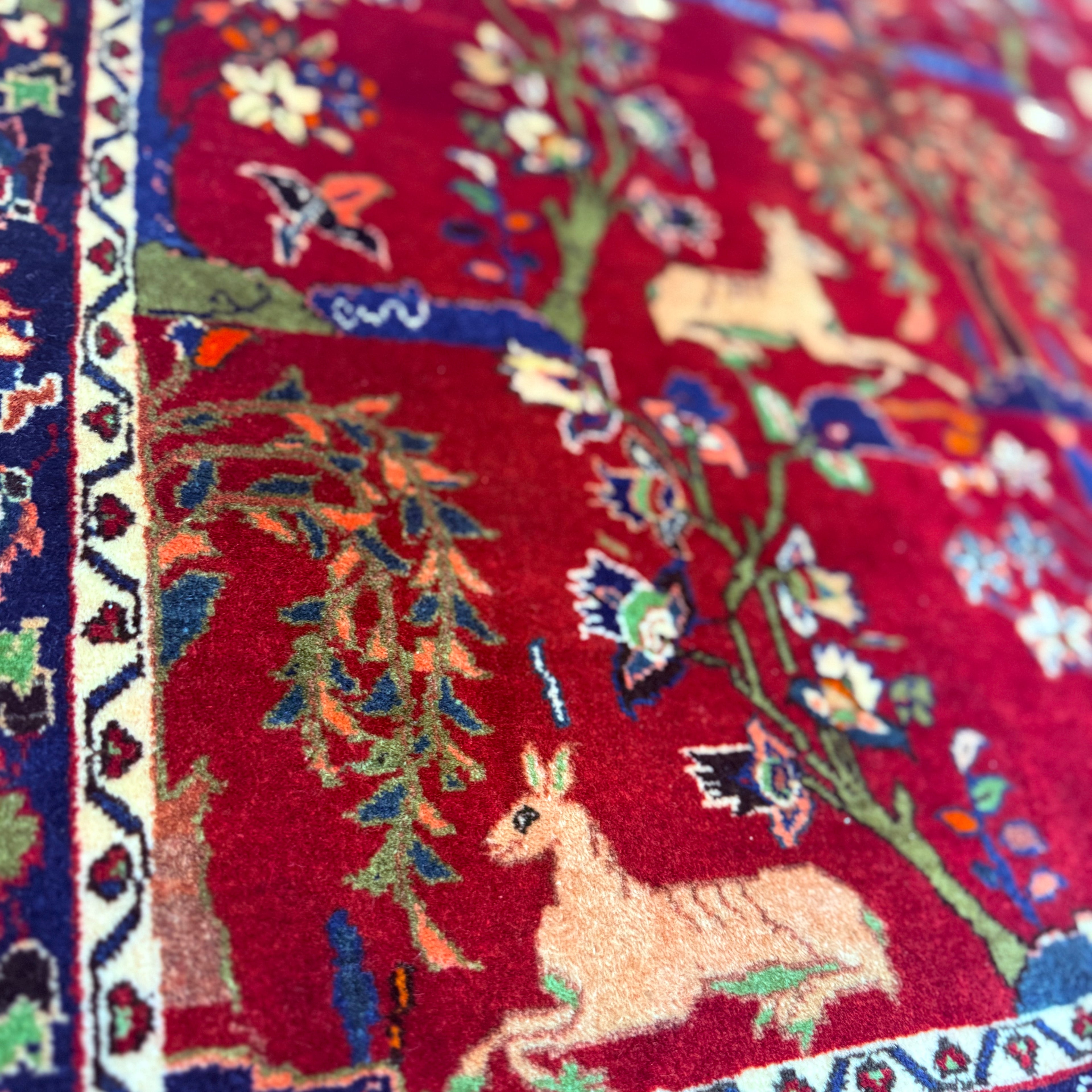 Close-up of a colorful rug with deer and floral patterns on a red background