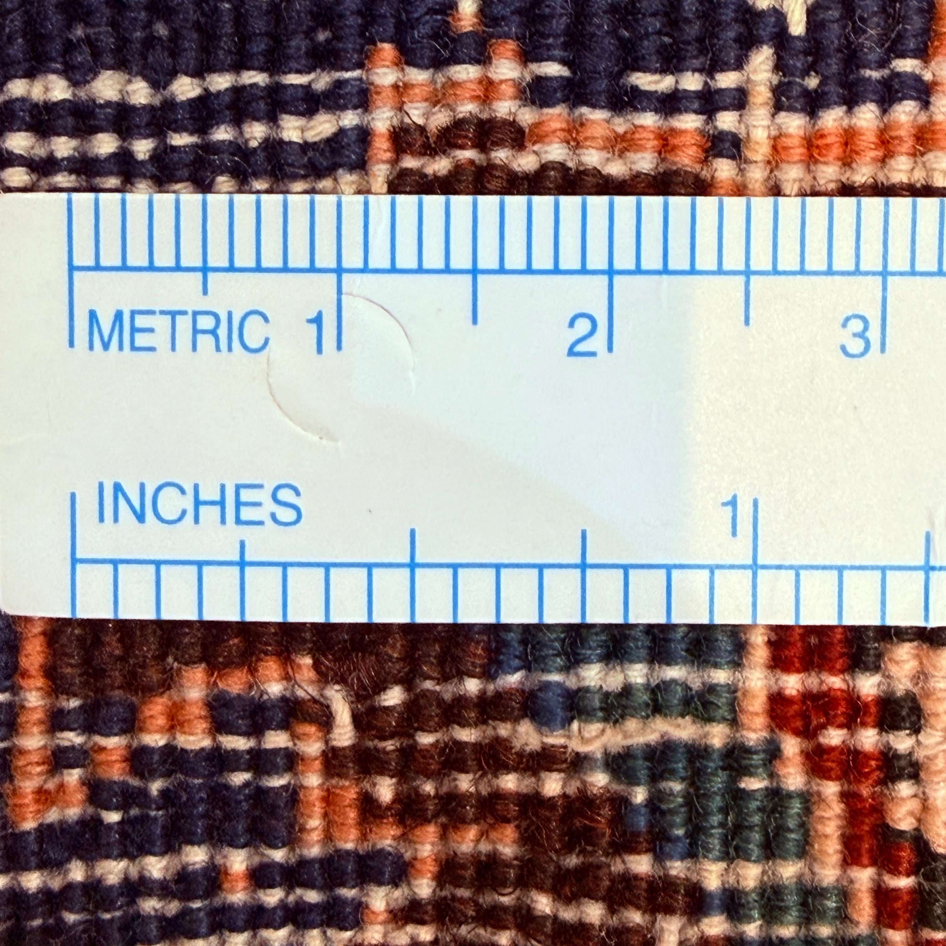 Close-up of a textured fabric with a ruler overlay showing measurements in both metric and inches.