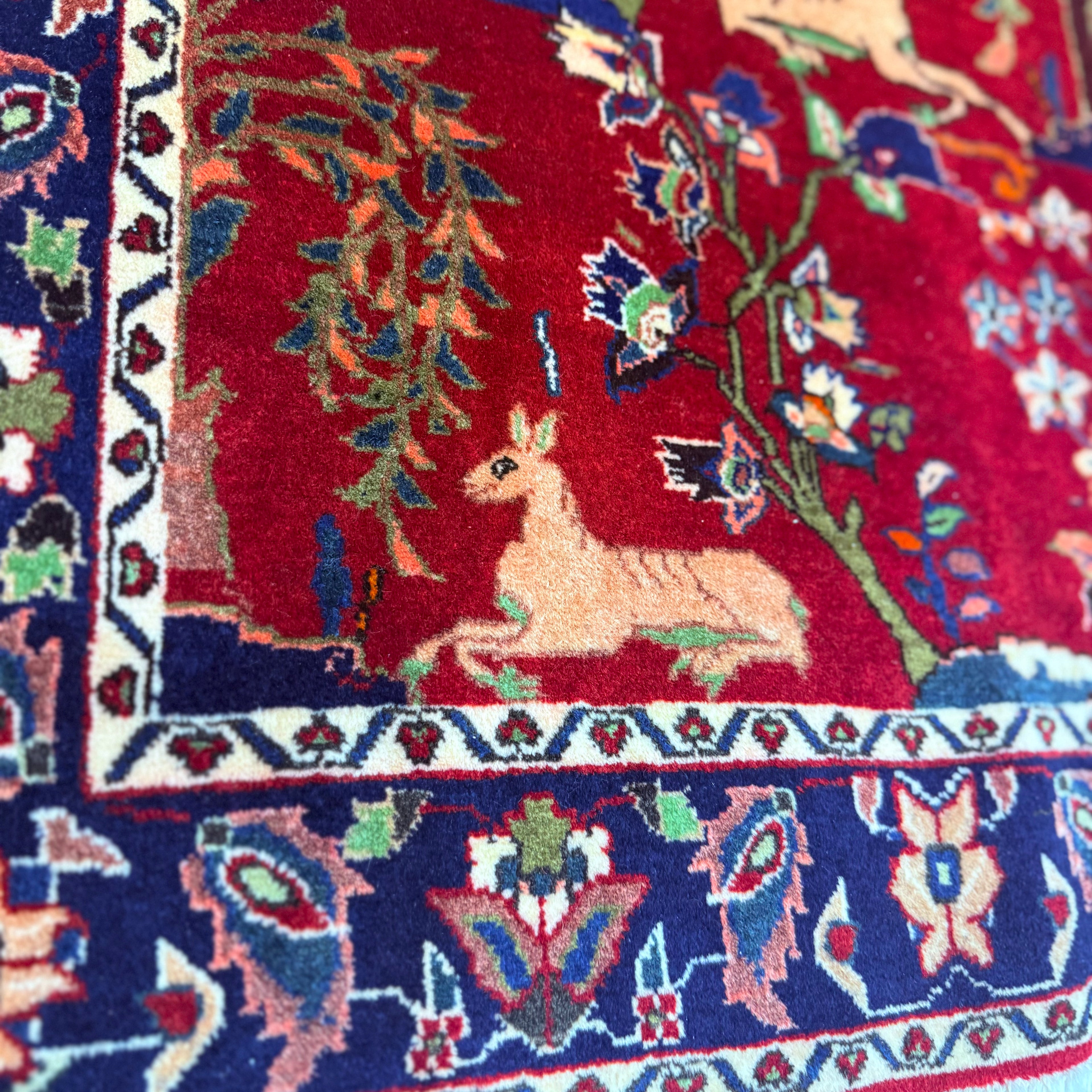 Close-up of a colorful rug with intricate patterns and a deer design on a red background.