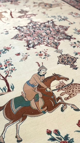A close-up of an ornate patterned rug featuring a central illustration of a rider on a brown horse, with floral motifs and a spotted animal on a cream background.