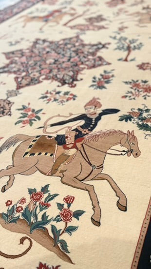 A close-up of a patterned rug featuring a detailed scene of a rider on a horse, surrounded by floral motifs and trees on a cream-colored background.