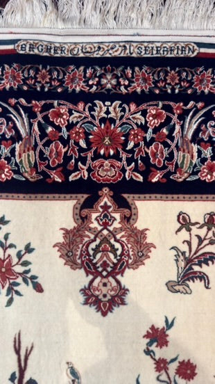 Close-up of an ornate patterned rug with a cream field, dark navy border, and red, green, and beige floral motifs.
