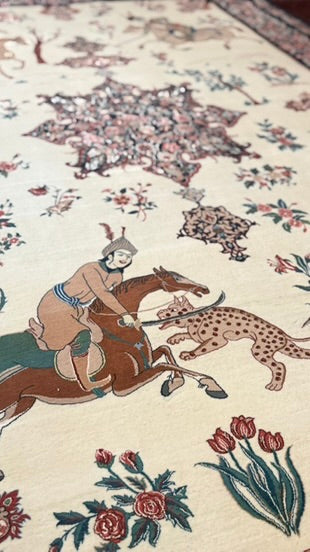 Close-up of an ornate patterned rug with a cream background, featuring a central figure riding a brown horse while chasing a spotted animal, surrounded by floral motifs and decorative medallions.