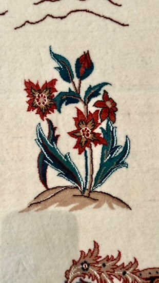 Close-up of a woven textile featuring a stylized floral motif with red flowers, teal-blue leaves, and a tan base on an off-white background.