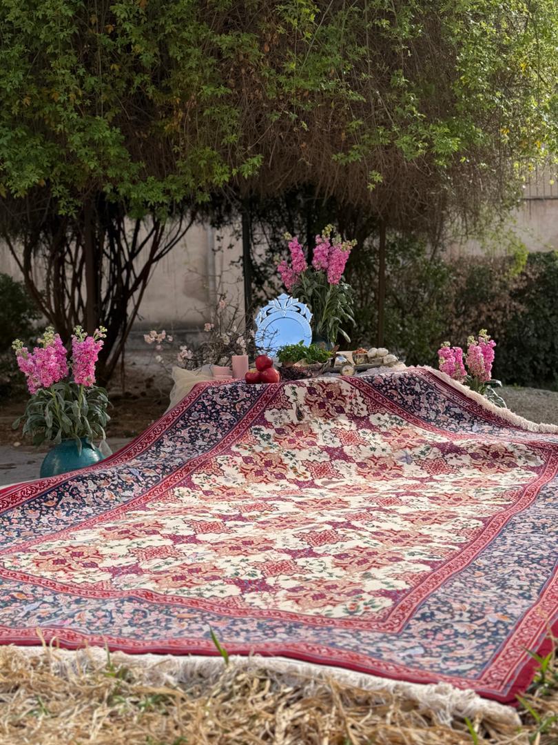 Decorative rug on grass with flowers and a decorative plate in the background
